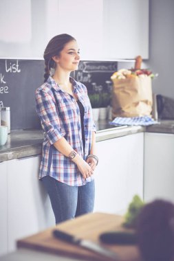 Kollarını mutfak arka planında kavuşturmuş genç bir kadının portresi.