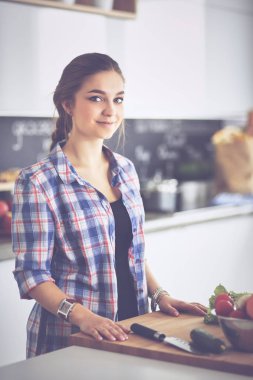 Masanın yanındaki mutfakta sebze doğrayan genç bir kadın.
