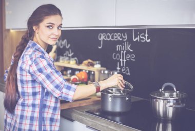 Mutfakta sobanın yanında duran genç bir kadın.