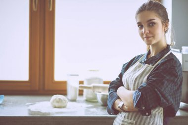 Güzel bir kadın mutfakta pasta pişiriyor. Masanın yanında duruyor.