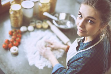 Güzel bir kadın mutfakta pasta pişiriyor. Masanın yanında duruyor.