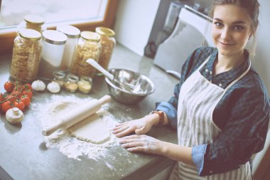 Güzel bir kadın mutfakta pasta pişiriyor. Masanın yanında duruyor.