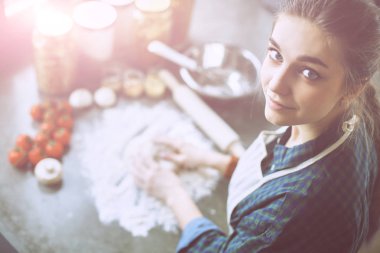 Güzel bir kadın mutfakta pasta pişiriyor. Masanın yanında duruyor.