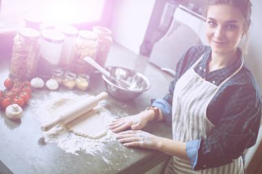 Güzel bir kadın mutfakta pasta pişiriyor. Masanın yanında duruyor.