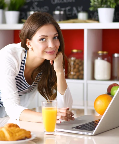 Attraente giovane donna che utilizza il computer portatile e seduto in cucina — Foto Stock