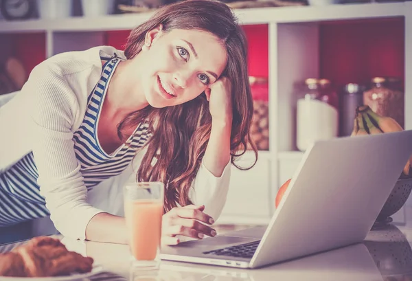 Attractive young woman using laptop and sitting in the kitchen — Stock Photo, Image