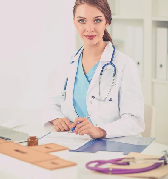 Güzel, genç, gülümseyen bayan doktor masada oturuyor ve yazıyor.. — Stok fotoğraf