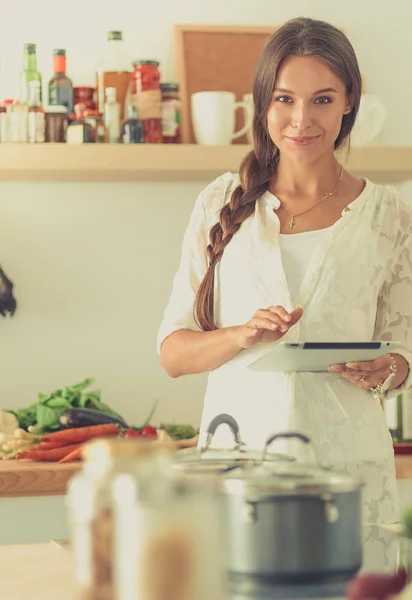 Young woman using a tablet computer to cook in her kitchen — Stock Photo, Image