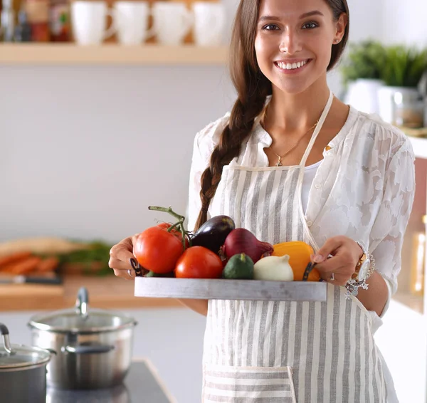 Улыбающаяся молодая женщина держит овощи стоя на кухне — стоковое фото