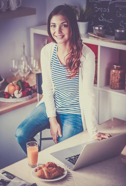 Dizüstü bilgisayar kullanarak ve mutfakta oturmuş çekici genç kadın — Stok fotoğraf