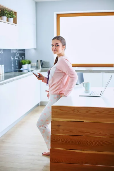 Mujer usando el teléfono móvil de pie en la cocina moderna — Foto de Stock