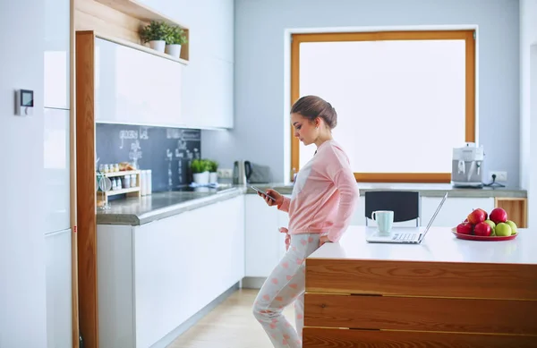 Mujer usando el teléfono móvil de pie en la cocina moderna — Foto de Stock