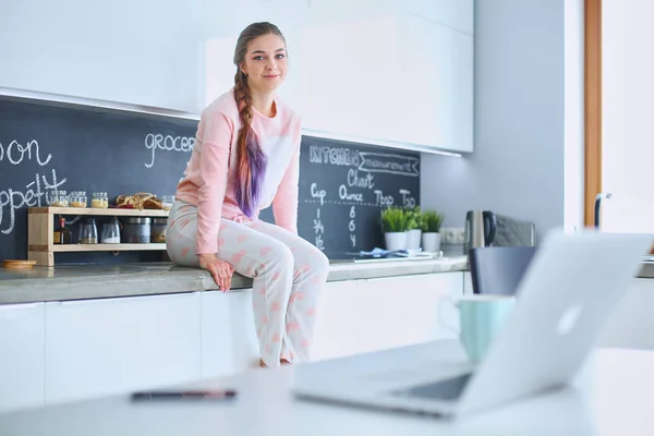 Jonge vrouw zittend op de tafel in de keuken — Stockfoto