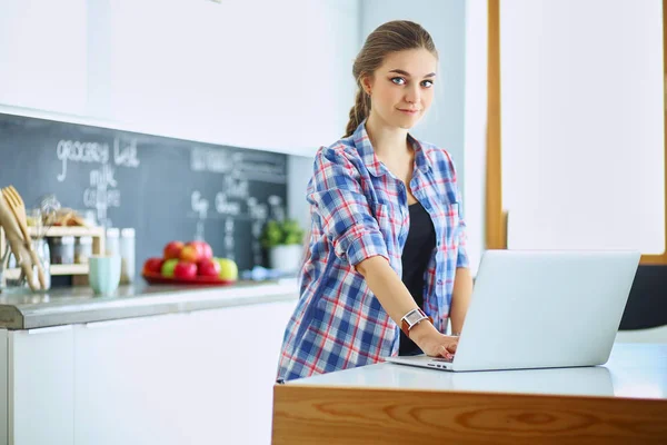 Jeune femme debout dans la cuisine en utilisant un ordinateur portable — Photo