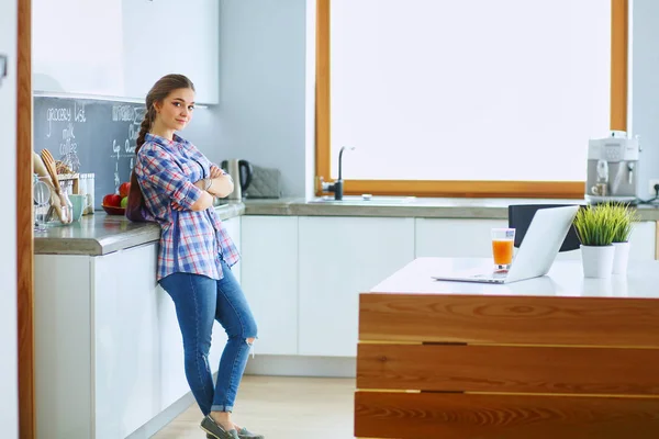 Retrato de mujer joven de pie con los brazos cruzados contra el fondo de la cocina — Foto de Stock