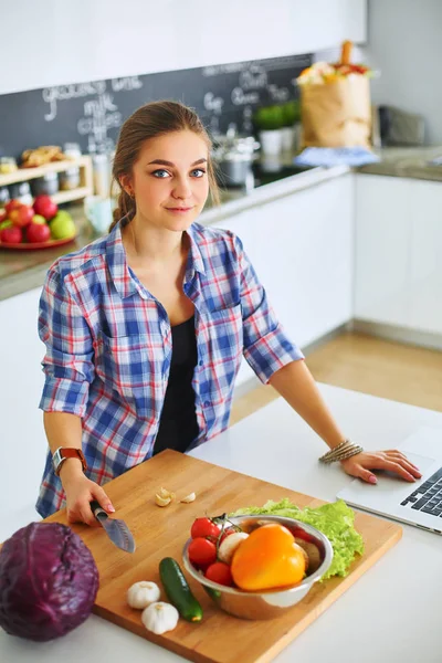 Masanın yanındaki mutfakta sebze doğrayan genç bir kadın.