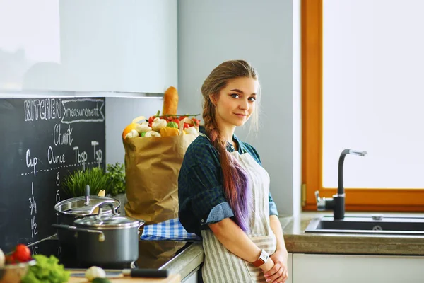 Egy fiatal nő áll a tűzhely mellett a konyhában. — Stock Fotó