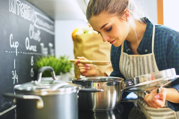 Ung kvinna matlagning i sitt kök står nära spis — Stockfoto