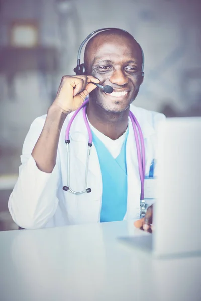 Porträt eines jungen männlichen Arztes, der ein Headset trägt, während er Computer am Schreibtisch in der Klinik benutzt — Stockfoto