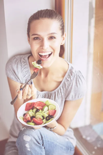 En vacker flicka äter hälsosam mat, sitter nära fönstret — Stockfoto