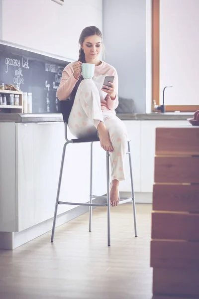 使用移动电话坐在现代厨房的女人 — 图库照片