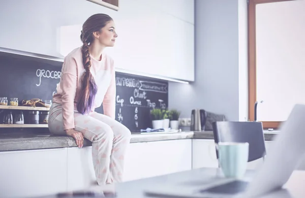 Jonge vrouw zittend op de tafel in de keuken — Stockfoto