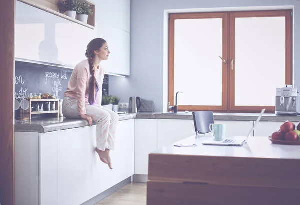 Jonge vrouw zittend op de tafel in de keuken — Stockfoto