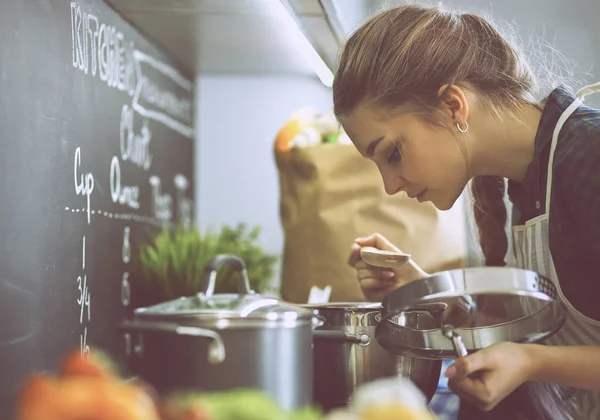 Mujer joven parada junto a la estufa en la cocina — Foto de Stock