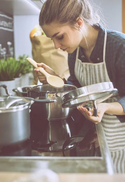 Молодая женщина готовит на кухне, стоя рядом с плитой — стоковое фото