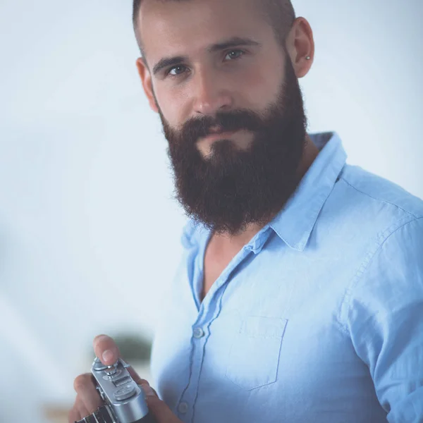 Young beard man holding a camera while standing against white background — Stock Photo, Image