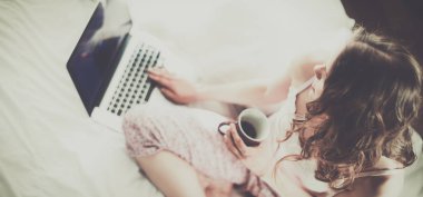 Dizüstü bilgisayar ile yatakta oturan genç güzel kadın