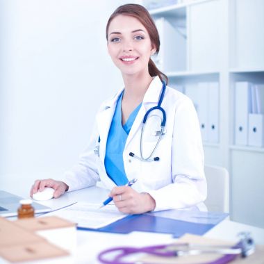 Güzel, genç, gülümseyen bayan doktor masada oturuyor ve yazıyor..