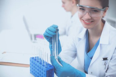 Kadın araştırmacı, beyaz arka planda izole edilmiş ilaç şişeleri ve mataralarla çevrili.