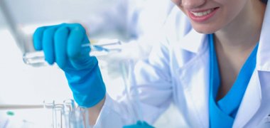 Kadın araştırmacı, beyaz arka planda izole edilmiş ilaç şişeleri ve mataralarla çevrili.