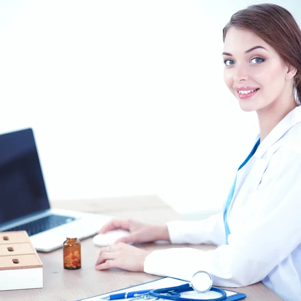 Schöne junge lächelnde Ärztin sitzt am Schreibtisch und schreibt. — Stockfoto