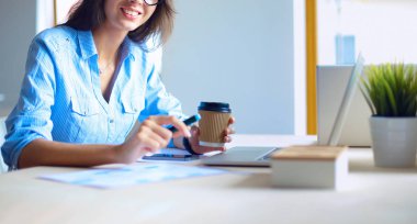 Ofis masasında dizüstü bilgisayarıyla oturan genç bir kadın.