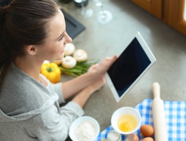 Tablette tarifi takip eden bir kadın evde yemek pişiriyor.
