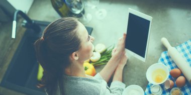 Tablette tarifi takip eden bir kadın evde yemek pişiriyor.