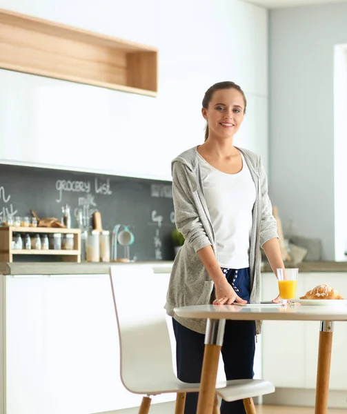 Mujer joven con jugo de naranja y tableta en la cocina —  Fotos de Stock