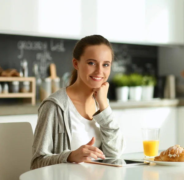 Ung kvinna med apelsinjuice och tablett i köket — Stockfoto