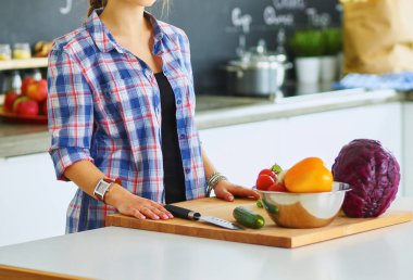 Masanın yanındaki mutfakta sebze doğrayan genç bir kadın.