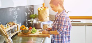 Masanın yanındaki mutfakta sebze doğrayan genç bir kadın.