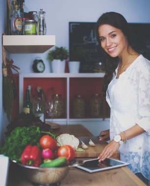 Mutfakta yemek yapmak için tablet bilgisayar kullanan genç bir kadın.