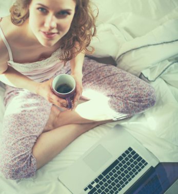 Dizüstü bilgisayar ile yatakta oturan genç güzel kadın