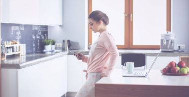 Cep telefonu ayakta modern mutfak kullanan kadın