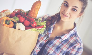 Elinde sebzeli alışveriş torbası tutan genç bir kadın.