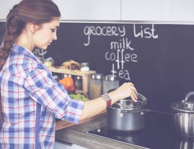 Mutfakta sobanın yanında duran genç bir kadın.