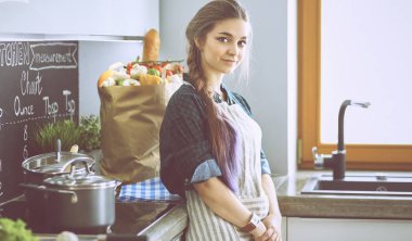 Mutfakta sobanın yanında duran genç bir kadın.