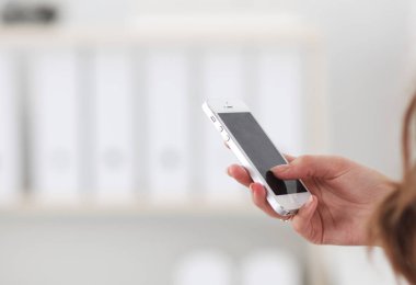 İş kadını ofiste akıllı telefonla mesaj gönderiyor.