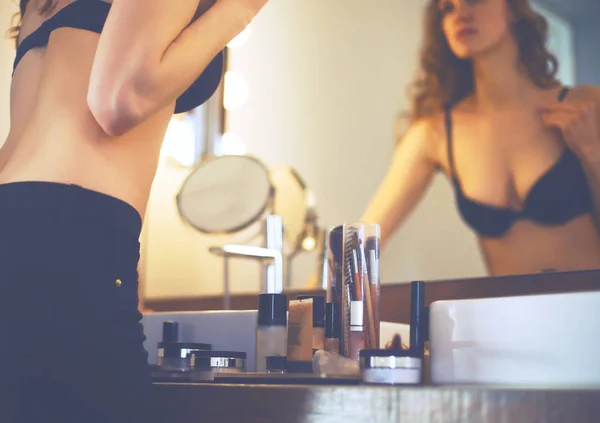 Mujer joven mirándose en el espejo en el baño — Foto de Stock